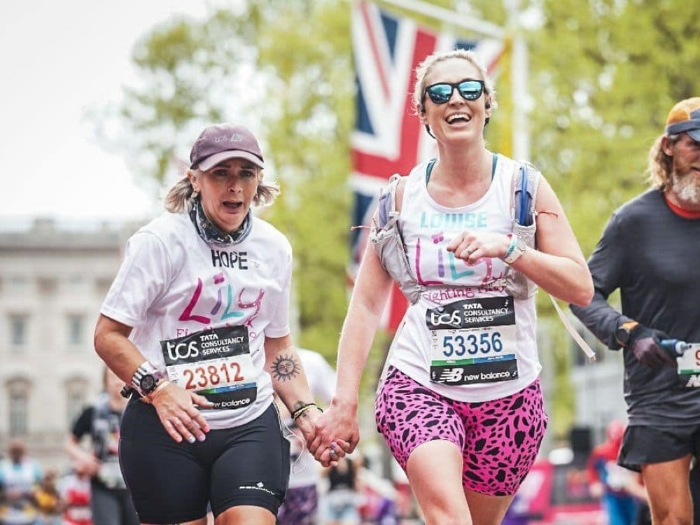 Two women in Lily vests holding hands, running and smiling