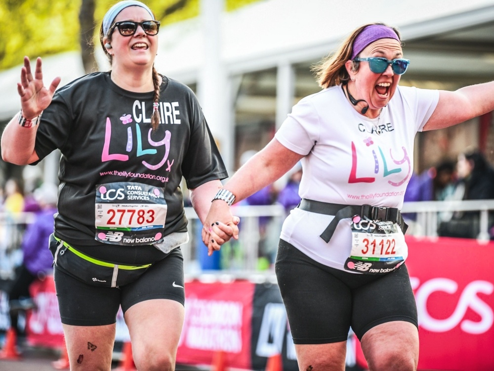 Two women in Lily Foundation tops holding hands and crossing the London Marathon finish line